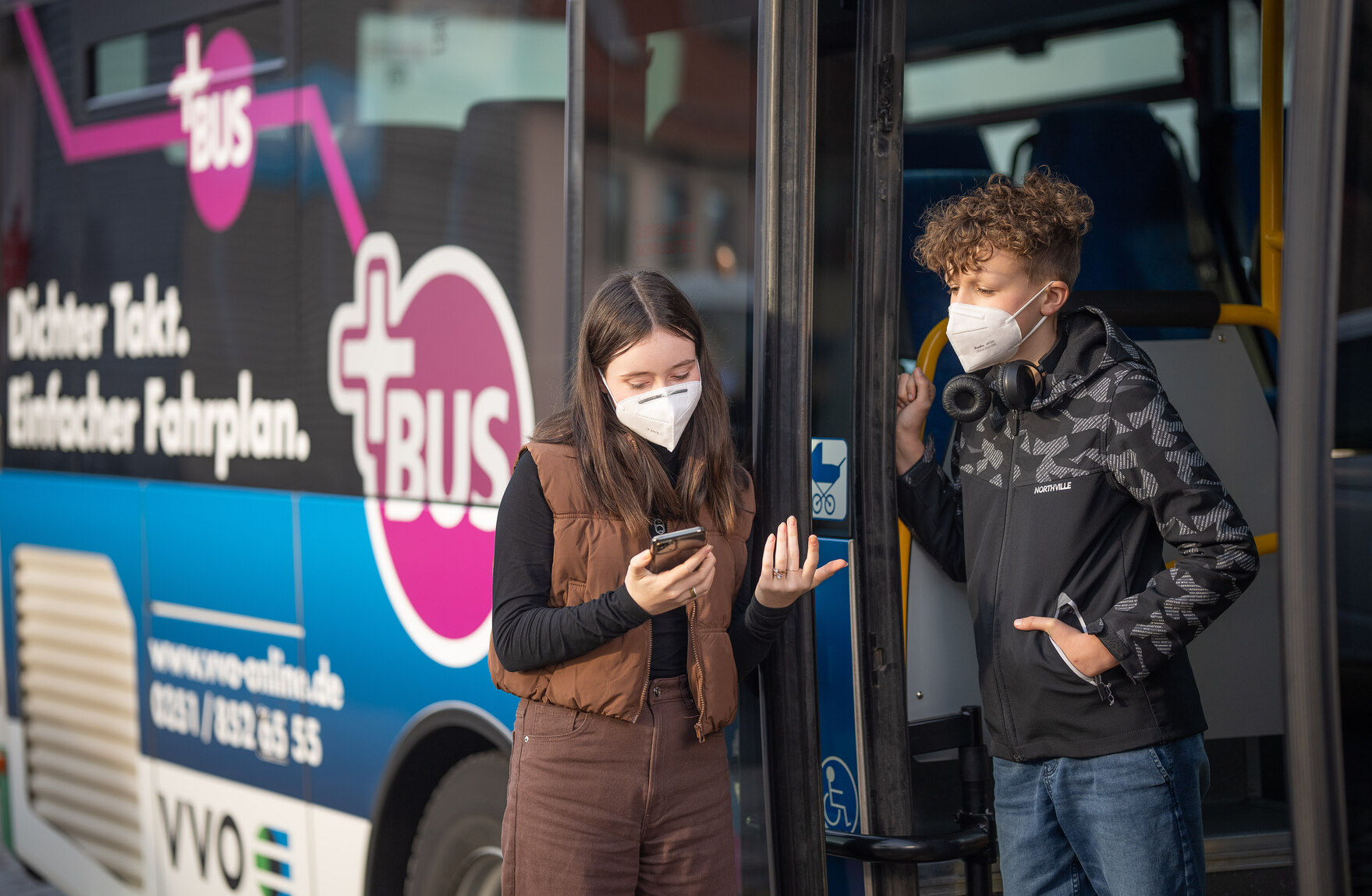 Zwei Jugendliche, ein Junge und ein Mädchen, stehen vor einem PlusBus.