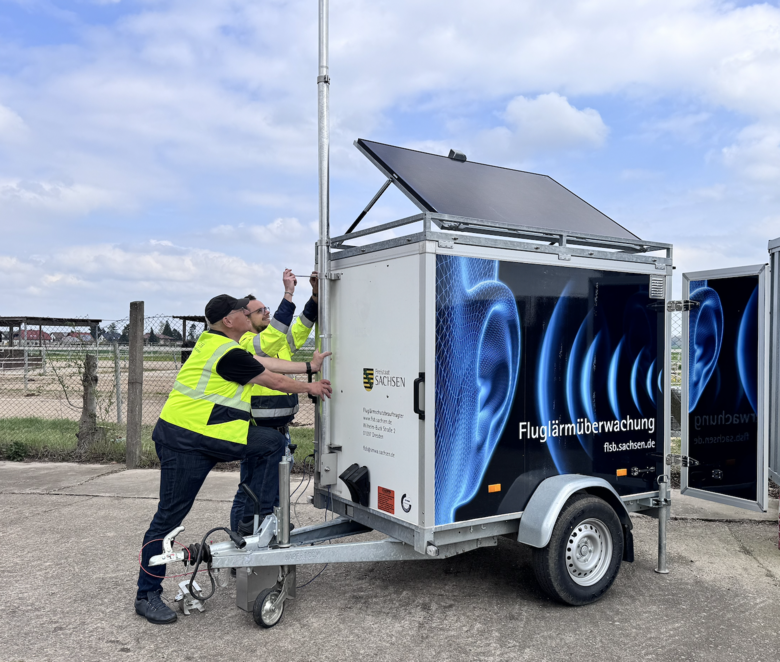 Eine Fluglärmmessanlage wird von zwei Herren aufgebaut und in Betrieb genommen
