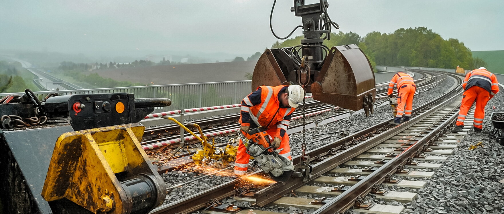 Drei Bauarbeiter bei Arbeiten auf einer Bahnstrecke.
