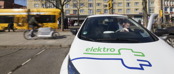 E-Auto mit Lastenfahrrad und Straßenbahn im Hintergrund.